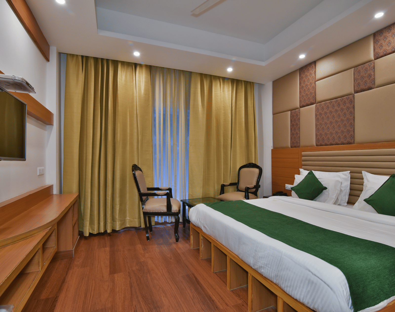 A large bed placed next to two chairs in the Deluxe Room at DLS Highland Resort and Spa, Mussoorie.